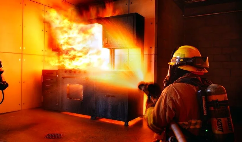 Firefighter suppressing a kitchen fire prop inside a custom flashover chamber training structure — Stump MFG, Modesto CA